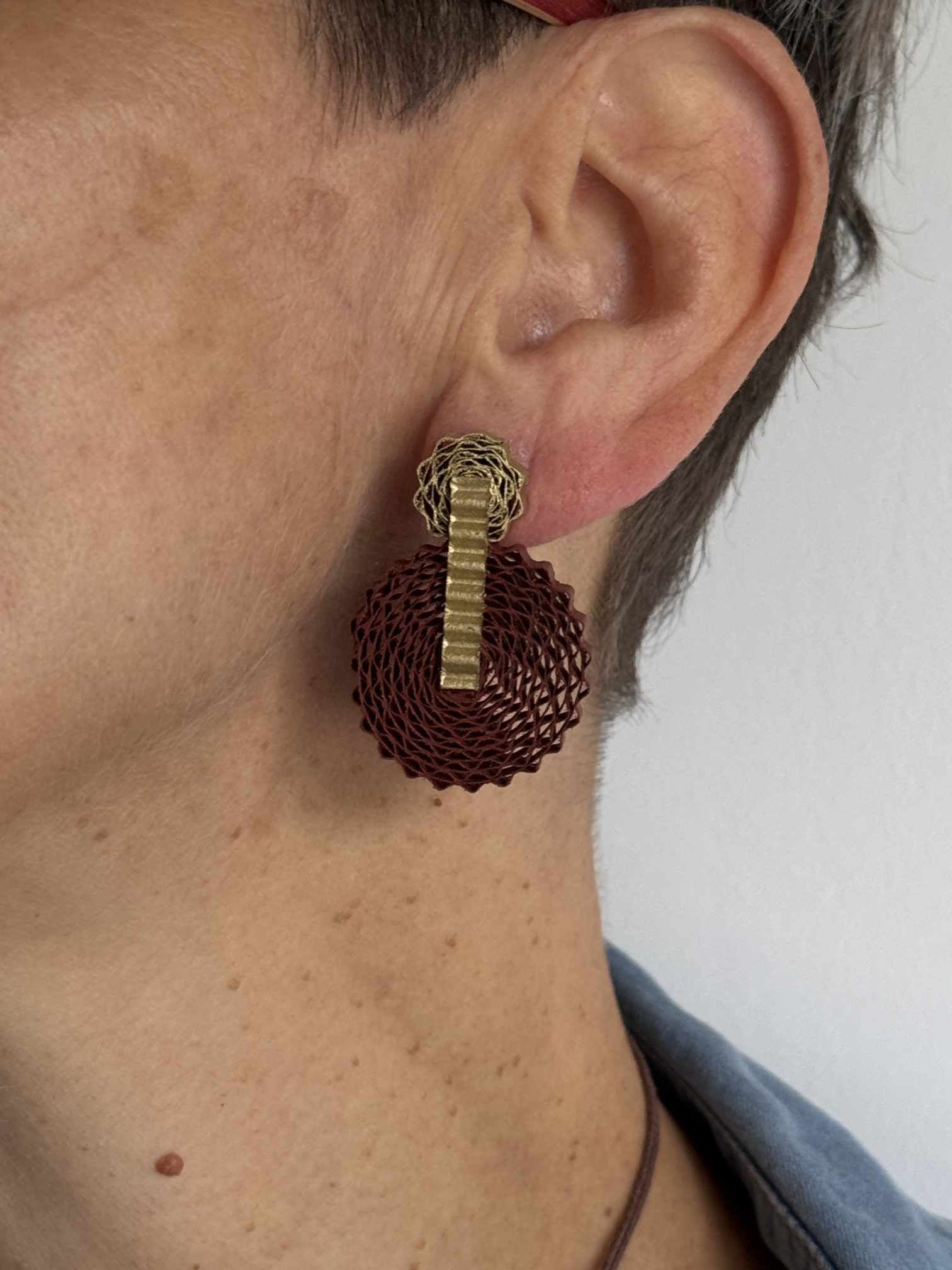 Gros plan sur une femme portant les boucles d'oreilles pendantes Corolle en carton recyclé terracotta et doré